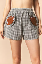 Black gingham ruffled football shorts by PEACH LOVE, showcasing the stylish ruffle detail and comfortable fit.