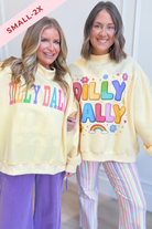 Two women modeling matching pale yellow sweatshirts with colorful 'DILLY DALLY' text and floral/rainbow graphics, paired with striped pants. A pink 'SMALL-2X' overlay appears in the top-left corner.