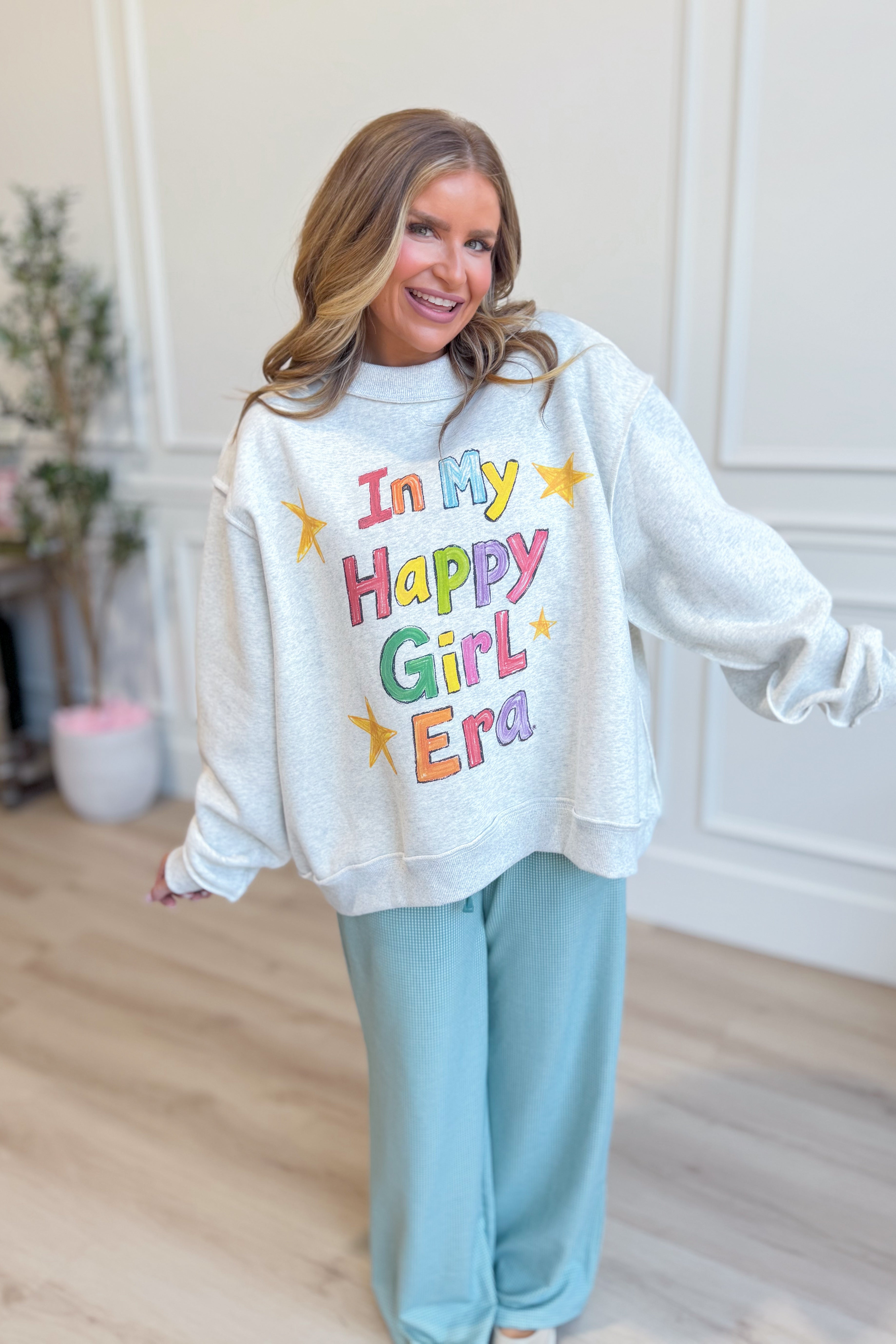 Reversible BUCKET LIST "In My Happy Girl Era" graphic sweatshirt in soft fabric, displayed on a hanger.