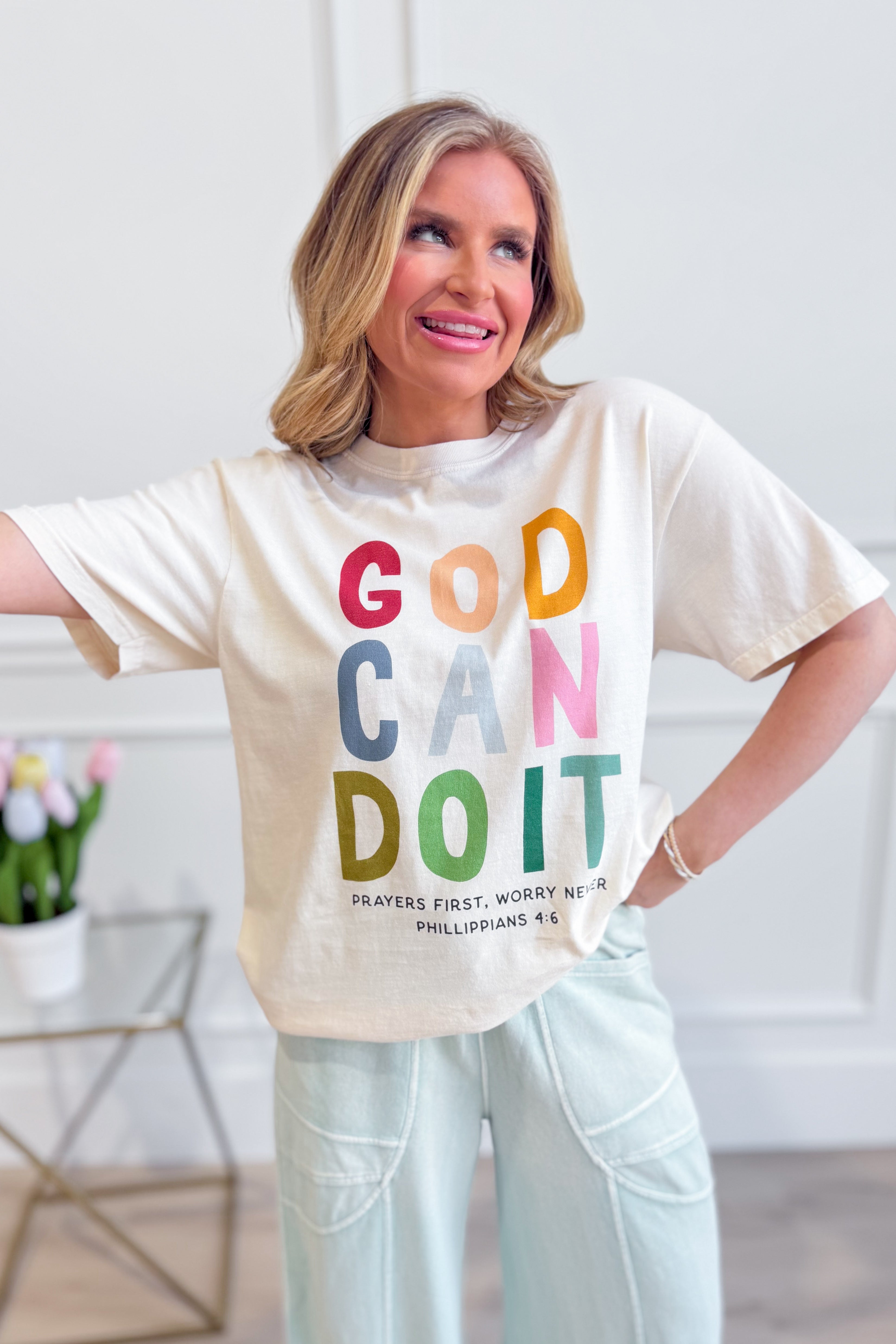 Poppy & Pine God Can Do It graphic T-shirt with bold text and vibrant design, casual fit, displayed on a hanger.